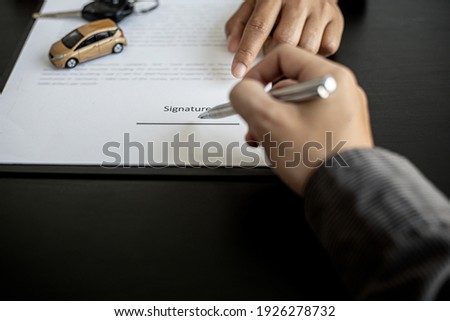 Close-up picture The renter is signing the car rental signature with the car rental company, with the staff explaining the details and terms of the car rental with the company. Concept of car rental.
