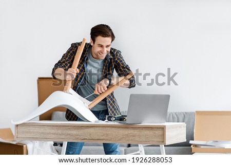 Hobby, furniture assembly and online instructions at home. Happy attractive young guy handyman screwing detail to chair, looking at laptop at manual in blog in living room interior, copy space Royalty-Free Stock Photo #1926288053