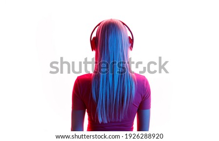Blue and red neon light. Young woman in modern headphones listening music. White background. Back view.