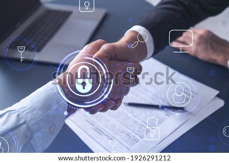 Handshake of two businessmen who enters into the contract to protect cyber security of international company. Padlock Hologram icons over the table with documents.