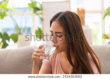 Young Asian woman drinking water and taking pill while sitting on sofa at home. Asian woman stressed and sick  Royalty-Free Stock Photo #1926303002