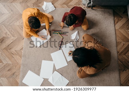 Happy african american mom teaching her sons to draw with pencils. Mother's day concept. Top view