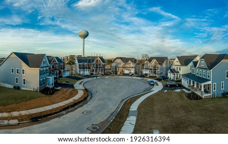 Aerial view of new construction street with luxury houses in cul-de-sac upper middle class neighborhood American real estate development in the USA with dreamy blue cloudy sky and water tower	
