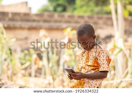 african kid using a smartphone. african child sitting alone outside viewing something on a phone Royalty-Free Stock Photo #1926334322