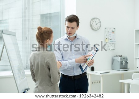Two young elegant accountants discussing financial data in document with diagrams and charts while man pointing at paper in office