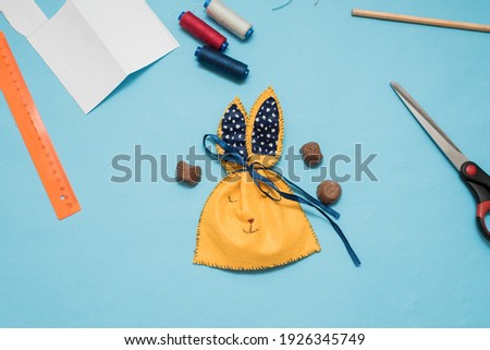 Step-by-step instructions: How to make an Easter bunny packaging for sweets. Children's art project. Happy Easter concept. Yellow bag for sweets for easter on a blue background