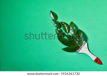 Creative composition of green leaves and paint brush on green background. Top view, flat lay. spring concept composition. Copy space.