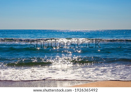The blue sea sparkling in the sun with a wave running on the sandy shore. Beautiful seascape. Travel and tourism..
