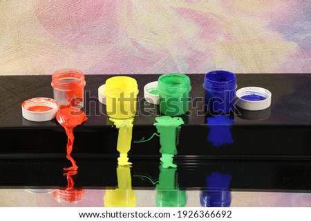 Cans of paint for drawing stand in the window on a black shelf in a row with a visible smeared red yellow green blue spot. Bright colorful image of objects for home and school creativity