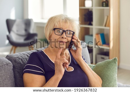 Happy mature woman in glasses talking to relatives on mobile sitting on couch at home. Wise mother-in-law having phone conversation with her daughter-in-law, listening to news and sharing advice Royalty-Free Stock Photo #1926367832