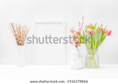 Home interior with easter decor. Mockup with a white frame and pink tulips in a vase on a light background
