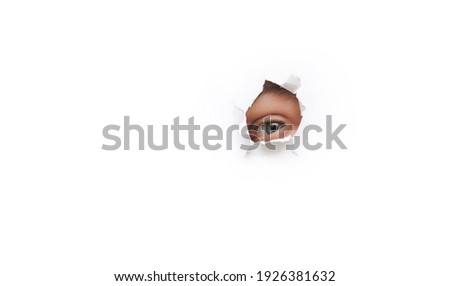 Left green eye. Voyeurism. The man is watching the wife. A curious look. Jealousy, spying on or overhearing the concept. Hole on white paper, copy space. Royalty-Free Stock Photo #1926381632