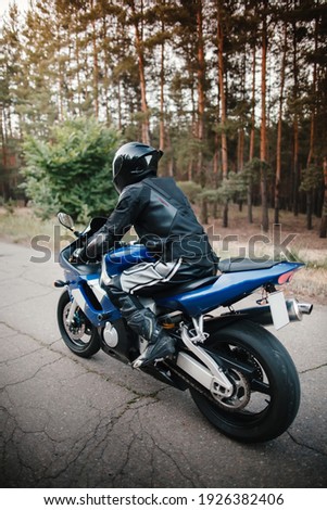 Rear view of motorcycle driver driving in helmet with blurred forest background