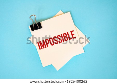 Text Impossible on sticky notes with copy space and paper clip isolated on red background.Finance and economics concept.