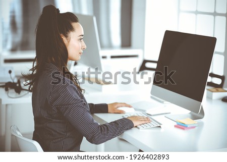 Business woman using computer at workplace in modern office. Brunette secretary or female lawyer smiling and looks happy. Working for pleasure and success