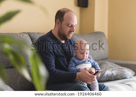 Caucasian father talking on mobile phone to work online with his newborn baby. Single dad taking care of his son. Happy family and work at home.