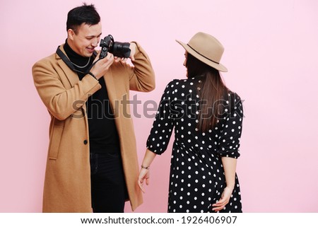 Man takes pictures of girl in hat on pink background. 