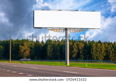 Big empty mockup Billboard along a highway with forest on background of blue sky with beautiful clouds. Royalty-Free Stock Photo #1926411632