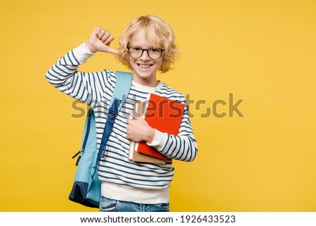 Smiling little male teen boy 10s years old in striped sweatshirt eyeglasses backpack hold school books pointing thumb on himself isolated on yellow background child studio portrait. Education concept