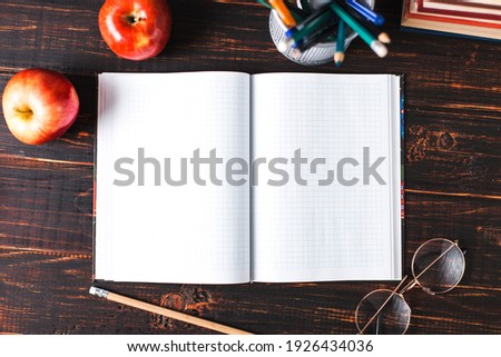 Notebook in a cage, pencil, apple and glasses on wooden table. Copy space.