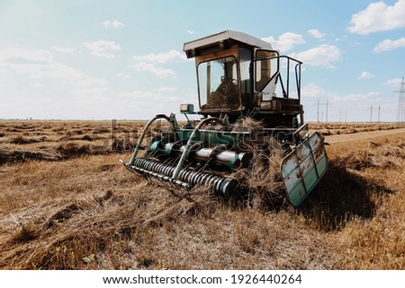 Old vintage agriculture harvester tractor machine vehicle remove dry hay grass at sunny summer field  Royalty-Free Stock Photo #1926440264