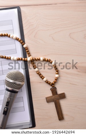 Vertical detail of Christian religious music with mic on sheet music book and cross background close up. Top view. Vertical composition.