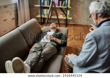 Calm young caucasian man lying on couch with closed eyes during psychotherapy session in office. Psychotherapy concept Royalty-Free Stock Photo #1926445154