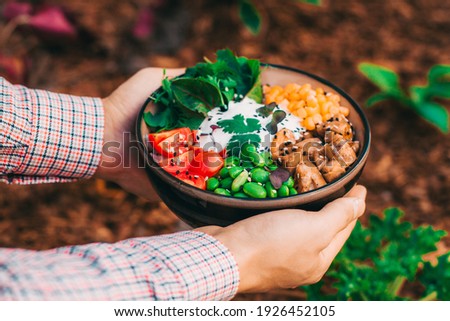 a dish of Hawaiian cuisine poke bowl with chicken is held in the hands. on a background of flowers