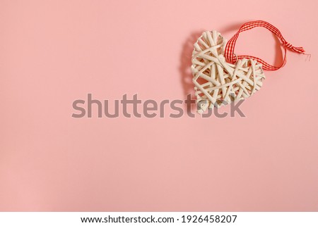White wicker heart with red ribbon on pink pastel background. Minimal flat lay  composition, romantic Valentines or International Women's day vintage concept