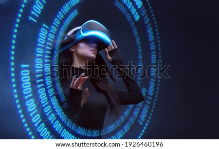 Woman on dark virtual reality background. Female using VR helmet. Augmented reality, future technology, game concept. Blue neon light. Futuristic holographic interface to display data. Royalty-Free Stock Photo #1926460196