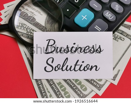 Phrase Business Solution written on white card with fake money,calculator and magnifying glass. Business and finance concept.