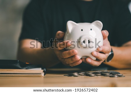 Man hand holding piggy bank on wood table, saving money wealth and financial concept, Business, finance, investment, Financial planning. Royalty-Free Stock Photo #1926572402