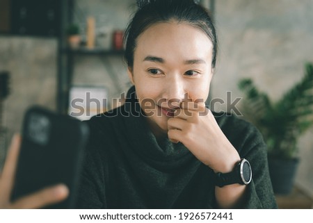 Young Asian Woman Taking Selfie by smartphone with smile sitting at living room or home working space. 