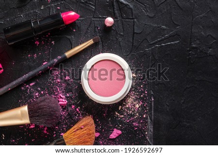 Makeup brushes, blush, and lipstick, overhead flat lay shot on a dark background with copy space