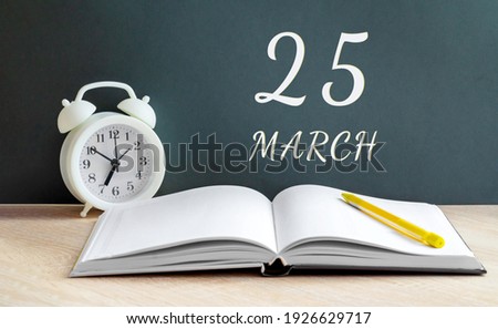 march 25. 25-th day of the month, calendar date. A white alarm clock, an open notebook with blank pages, and a yellow pencil lie on the table. Spring month, day of the year concept.