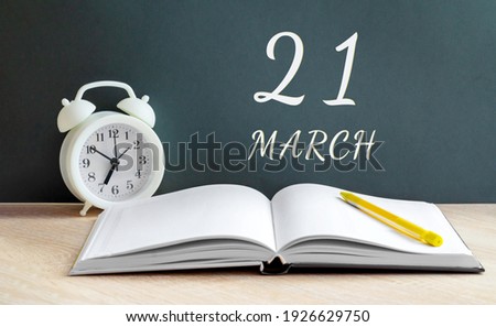 march 21. 21-th day of the month, calendar date. A white alarm clock, an open notebook with blank pages, and a yellow pencil lie on the table. Spring month, day of the year concept. Royalty-Free Stock Photo #1926629750