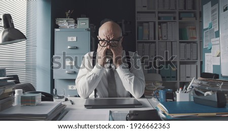 Tired stressed office worker sitting at desk and thinking, he is rubbing his eyes and feeling exhausted