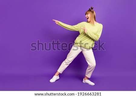 Photo of charming cute young woman dressed green pullover dancing looking pointing fingers empty space isolated purple color background