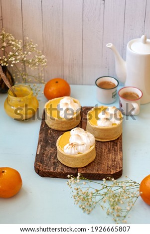 Tartlets with tangerine curd. Blue background. Flowers, coffee, tangerine. Side view.