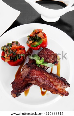 fresh red beef meat steak barbecue garnished vegetable salad and basil on white plate over black wooden table with bbq sauce in sauceboat