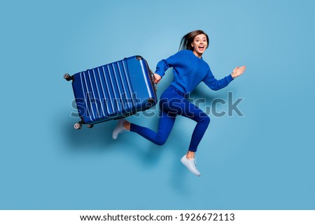 Full size photo of young happy positive good mood smiling girl run jump hold big luggage isolated on blue color background