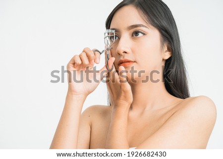 Beautiful young asian woman with eyelash curler on white background