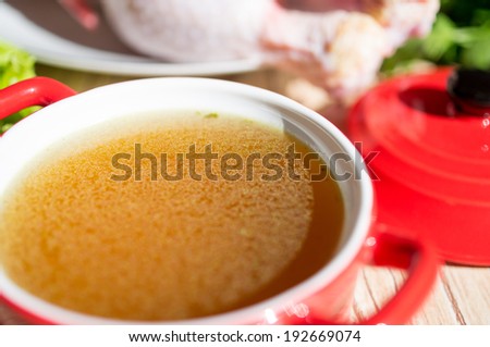 Chicken broth, bouillon, clear soup in a cup next to chicken and fresh herbs.