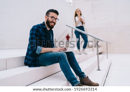 Portrait of successful male IT professional in optical spectacles smiling at camera, happy Caucasian blogger with modern laptop computer spending day for working remotely and create website