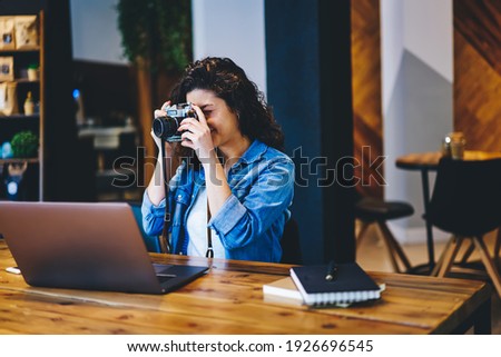 Skilled female photographer taking picture with vintage camera while working remotely in coffee shop, millennial woman focus for making photos using retro equipment during leisure time in cafe