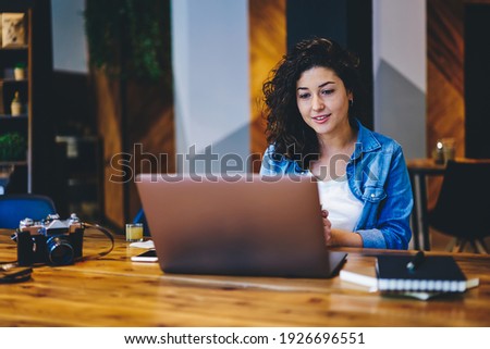 Caucasian female watching webinar video with information for media edition on laptop computer, skilled hipster girl reading web publication on netbook connecting to 4g internet in coworking space