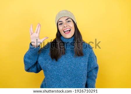 Young beautiful woman wearing blue casual sweater and wool hat doing hand symbol