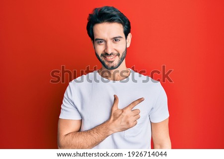 Young hispanic man wearing casual white tshirt cheerful with a smile on face pointing with hand and finger up to the side with happy and natural expression 