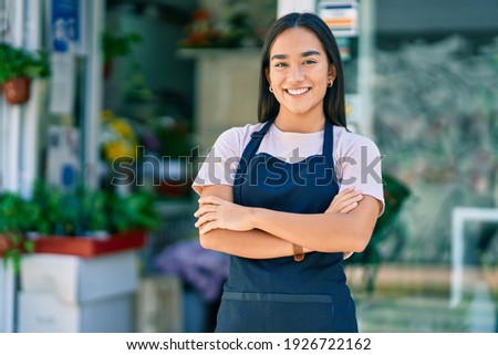 Young latin shopkeeper girl with arms crossed smiling happy standing at the florist Royalty-Free Stock Photo #1926722162