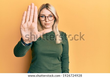 Young caucasian woman wearing casual clothes and glasses doing stop sing with palm of the hand. warning expression with negative and serious gesture on the face. 